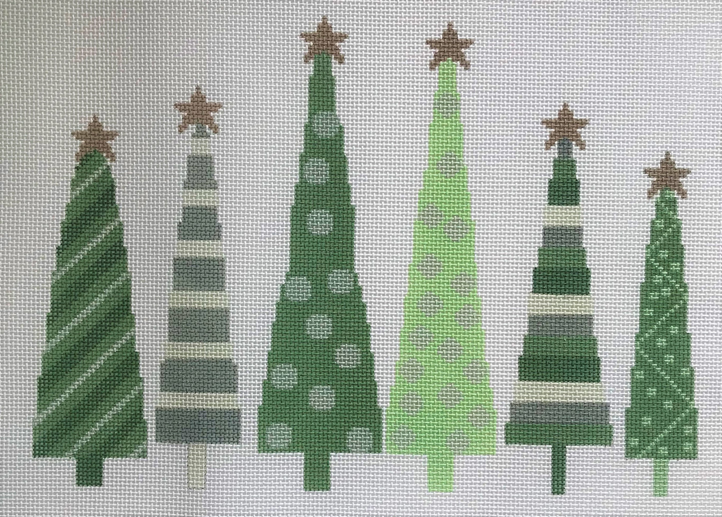 A Stitch in Time needlepoint canvas of six green and silver star-topped Christmas trees on a white background