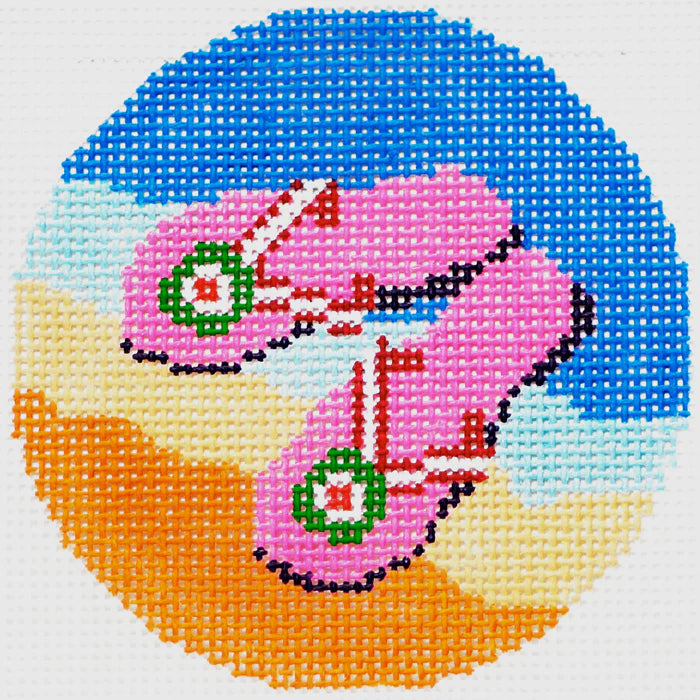 Lee's Needle Art round needlepoint canvas of a pair of pink sandals with green and red accents on a blue water and orange sand background.