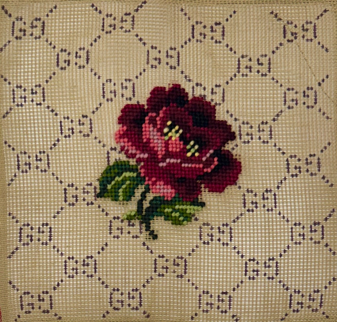 Jessica Tongel Designs needlepoint canvas of a an allover dark monogram pattern on a beige background with a central burgundy rose with green leaves.