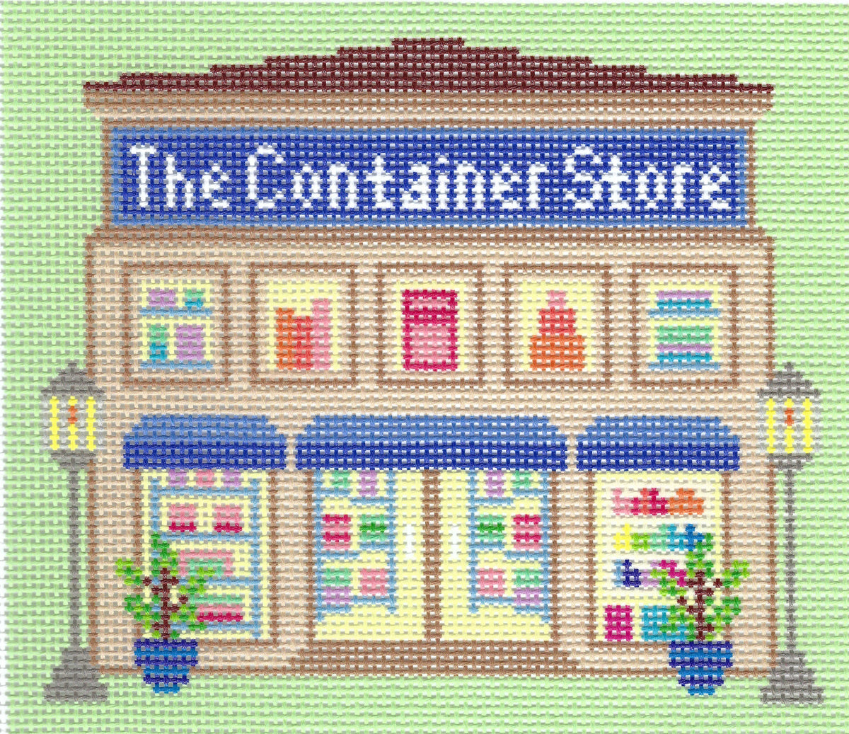 Haus of Toots needlepoint canvas design of a storefront reading "The Container Store" on a light green background, with beige building details, blue awnings and sign, colorful windows, and potted plants.