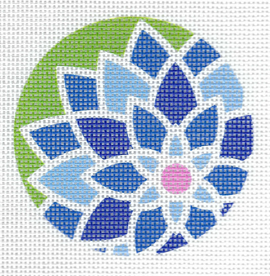 Pepperberry Designs round needlepoint canvas of a floral mandala design made of blue, navy, and light blue petals with a pink center on a green background.