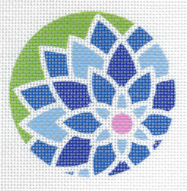 Pepperberry Designs round needlepoint canvas of a floral mandala design made of blue, navy, and light blue petals with a pink center on a green background.