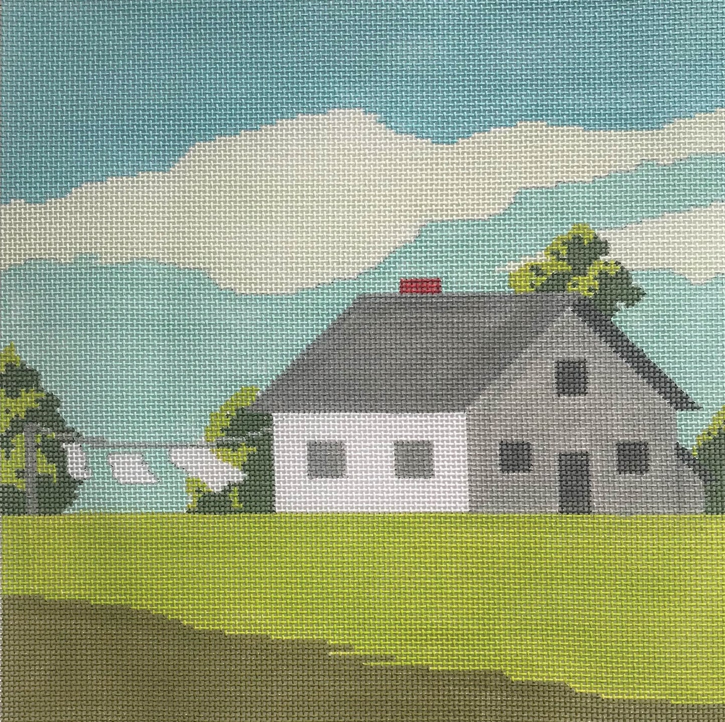 A Stitch in Time needlepoint canvas of a white house with laundry drying outside