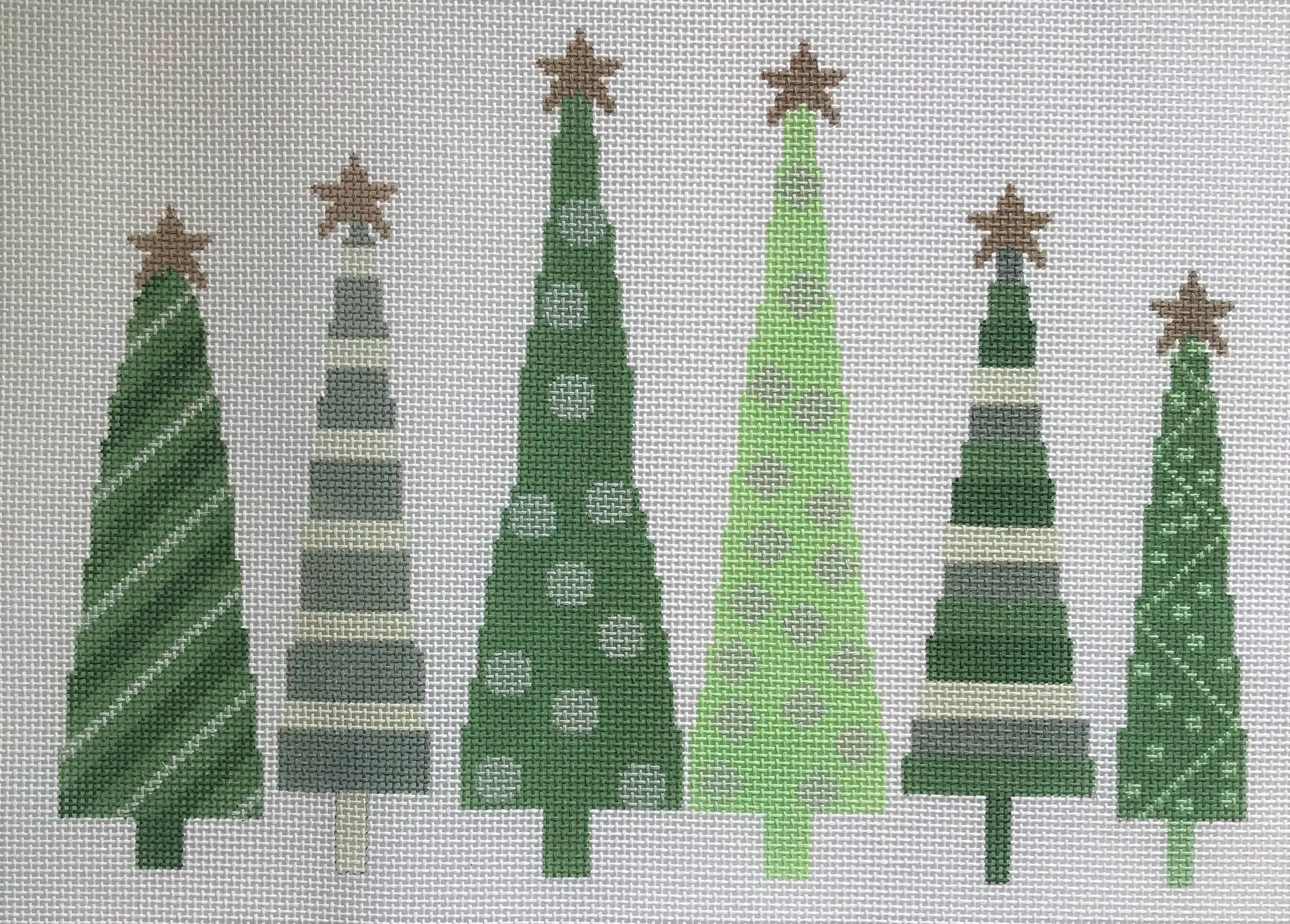 A Stitch in Time needlepoint canvas of six green and silver star-topped Christmas trees on a white background