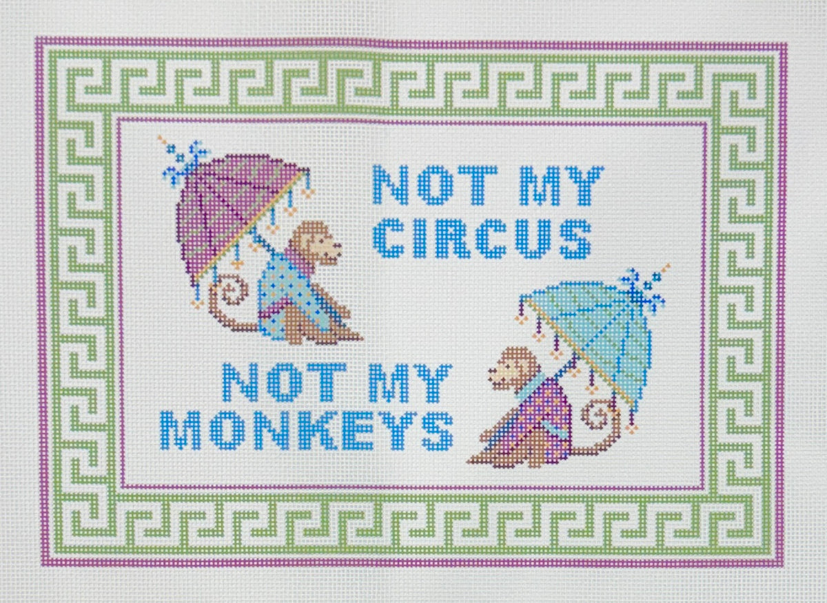 Needlepaint needlepoint canvas with the phrase 'NOT MY CIRCUS NOT MY MONKEYS' in blue lettering, flanked by two monkeys holding umbrellas, all enclosed in a decorative green, white, and pink border.