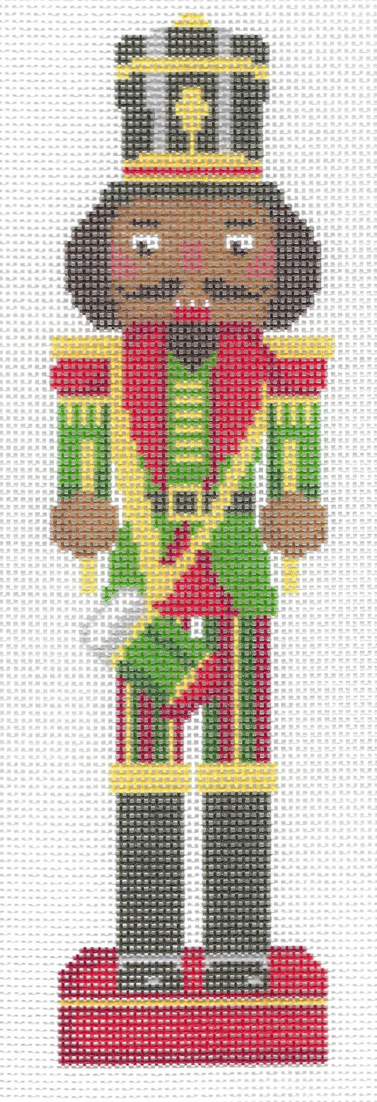 Spellbound Stitchery needlepoint canvas design of a traditional nutcracker soldier, featuring a black hair, a red, yellow, and green striped uniform, a gold and black hat, and a red base, set against a white background.