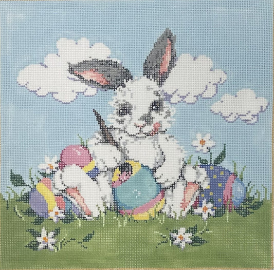 Sandra Gilmore needlepoint canvas of a bunny sitting in a field with four colorful Easter eggs with a light blue sky background featuring clouds. 
