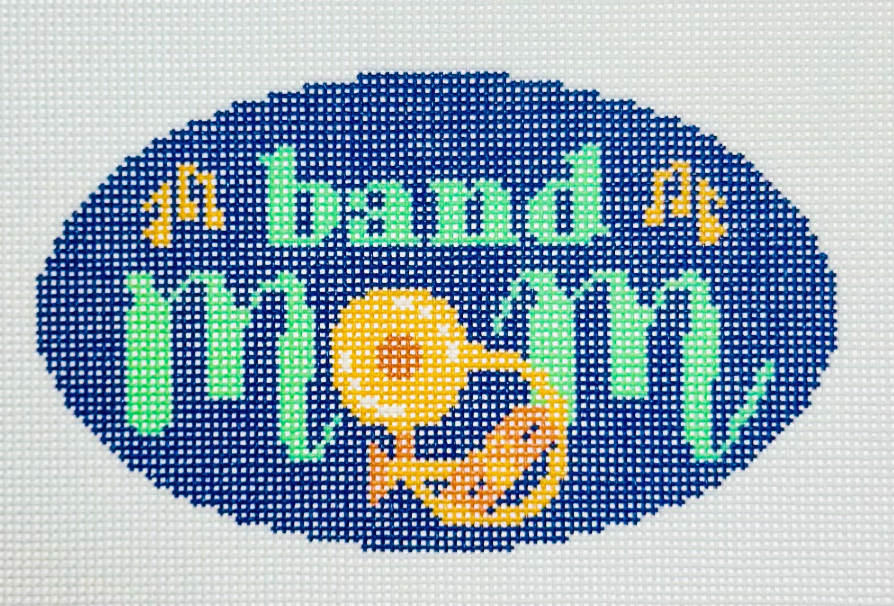 KCN Designers needlepoint canvas of 'Band Mom' with a brass instrument for the 'O' in 'mom' on a dark blue background.