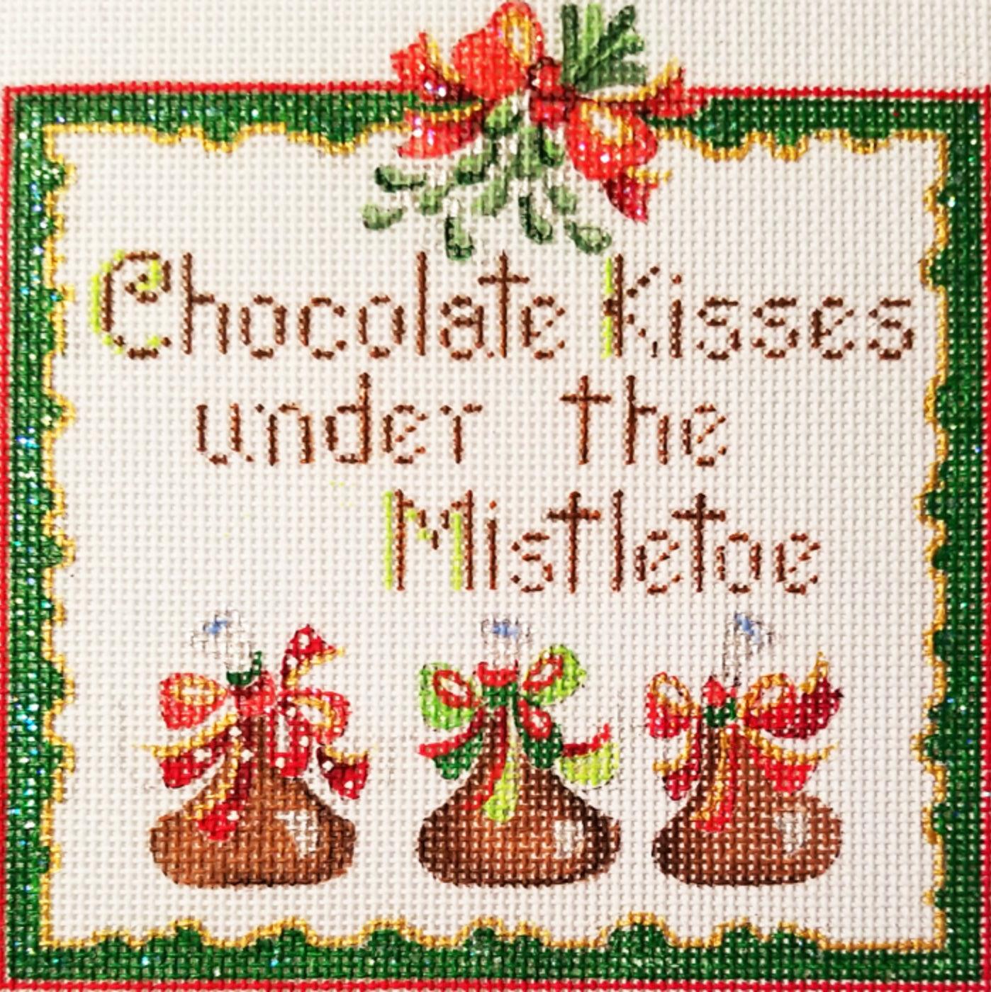 Linda Grayson square needlepoint canvas featuring the text 'Chocolate Kisses under the Mistletoe' with three decorated chocolate kisses and red bows beneath a holly motif, framed by a green border on a white background.