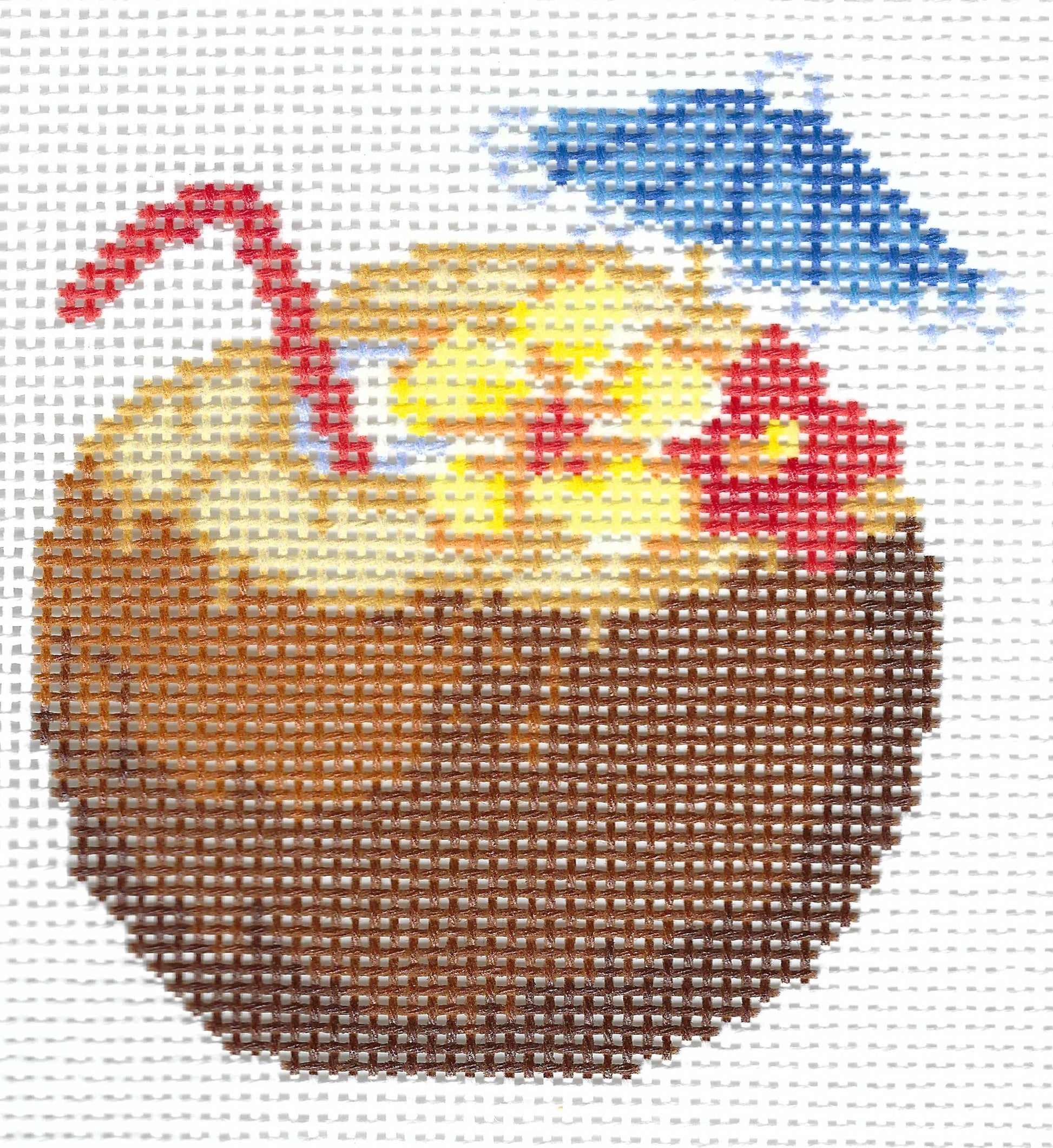 Needlepoint canvas of illustration of a brown coconut with a red straw, a blue umbrella, and red and yellow flowers on a white grid background.