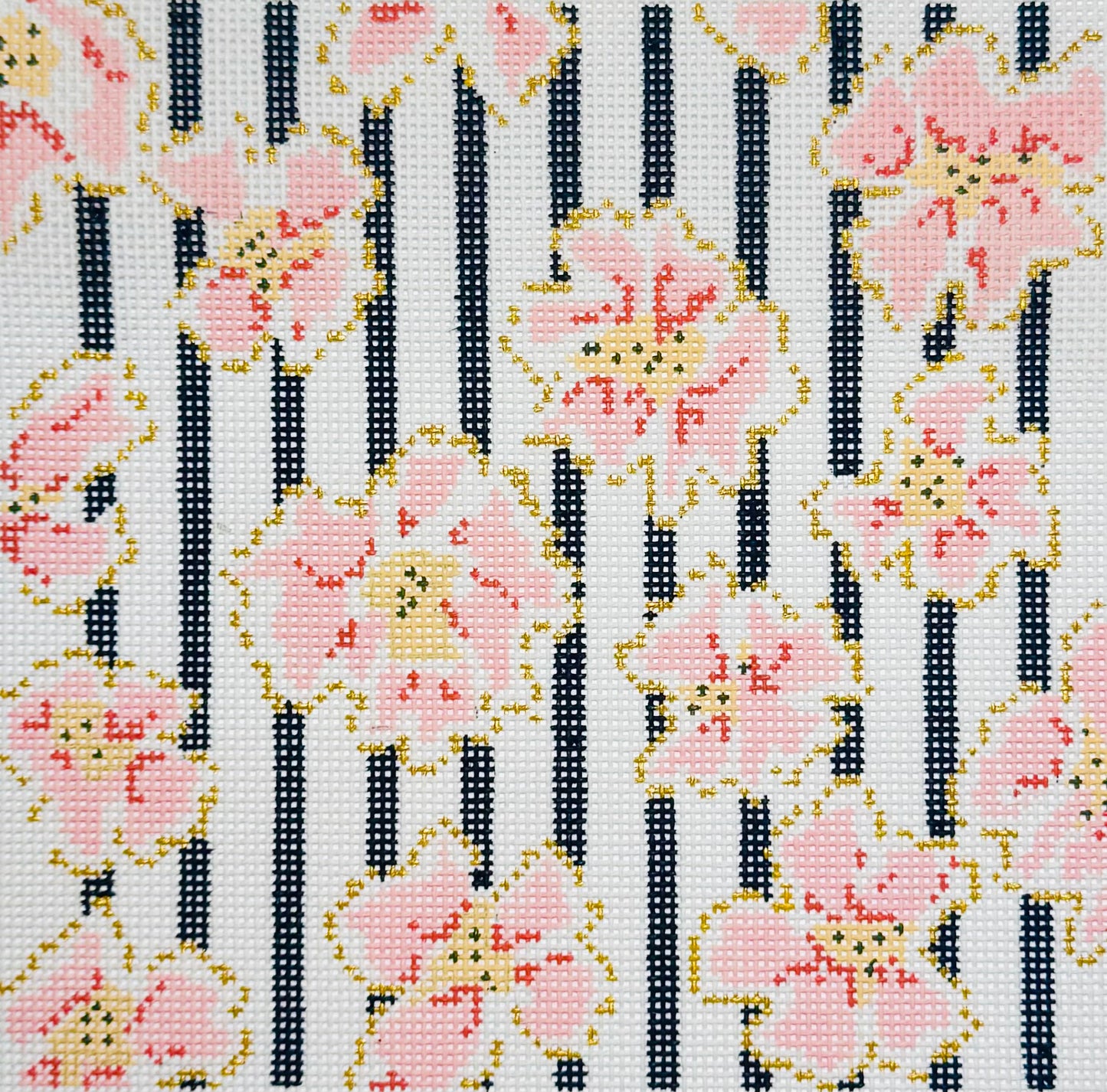 The Plum Stitchery needlepoint canvas of a floral pattern with coral and gold flowers and black vertical stripes on a white background.