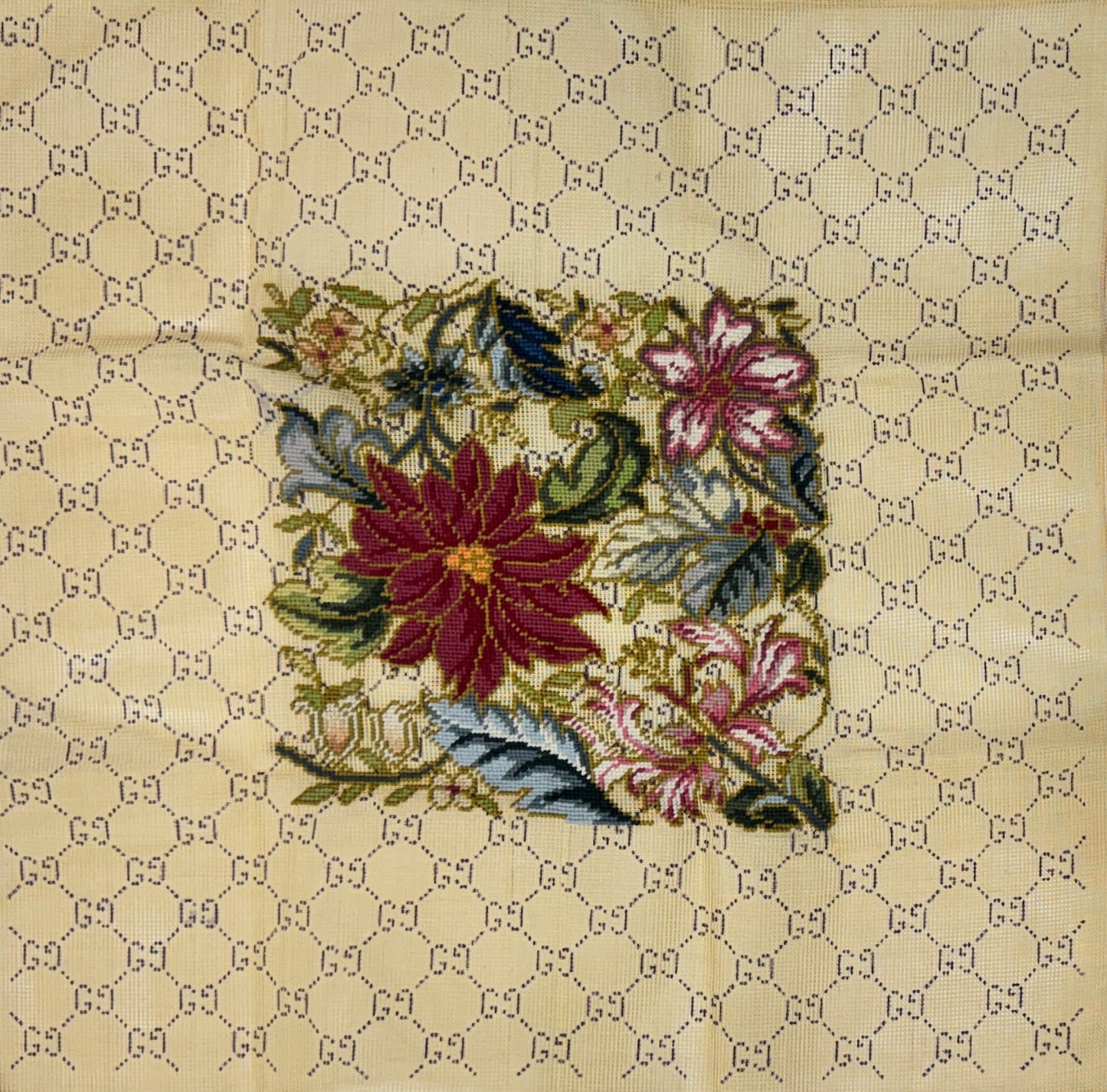 Jessica Tongel Designs needlepoint canvas featuring a central floral patch with red, pink, green, and blue flowers, set against a beige background patterned with a repeating interlocking GG pattern.