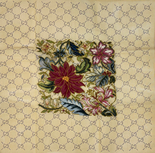 Jessica Tongel Designs needlepoint canvas featuring a central floral patch with red, pink, green, and blue flowers, set against a beige background patterned with a repeating interlocking GG pattern.