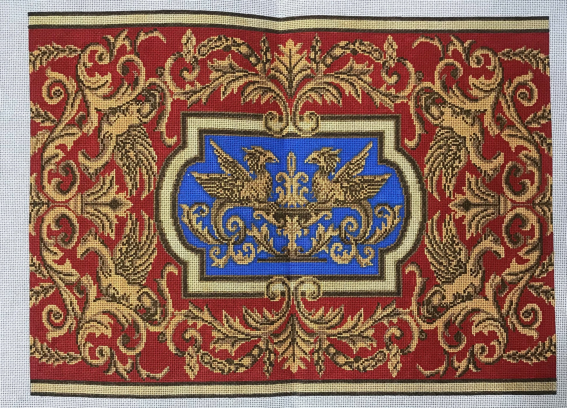 Point Of It All needlepoint canvas of gold intricate patterns on a red background and a central blue emblem with gold griffins.