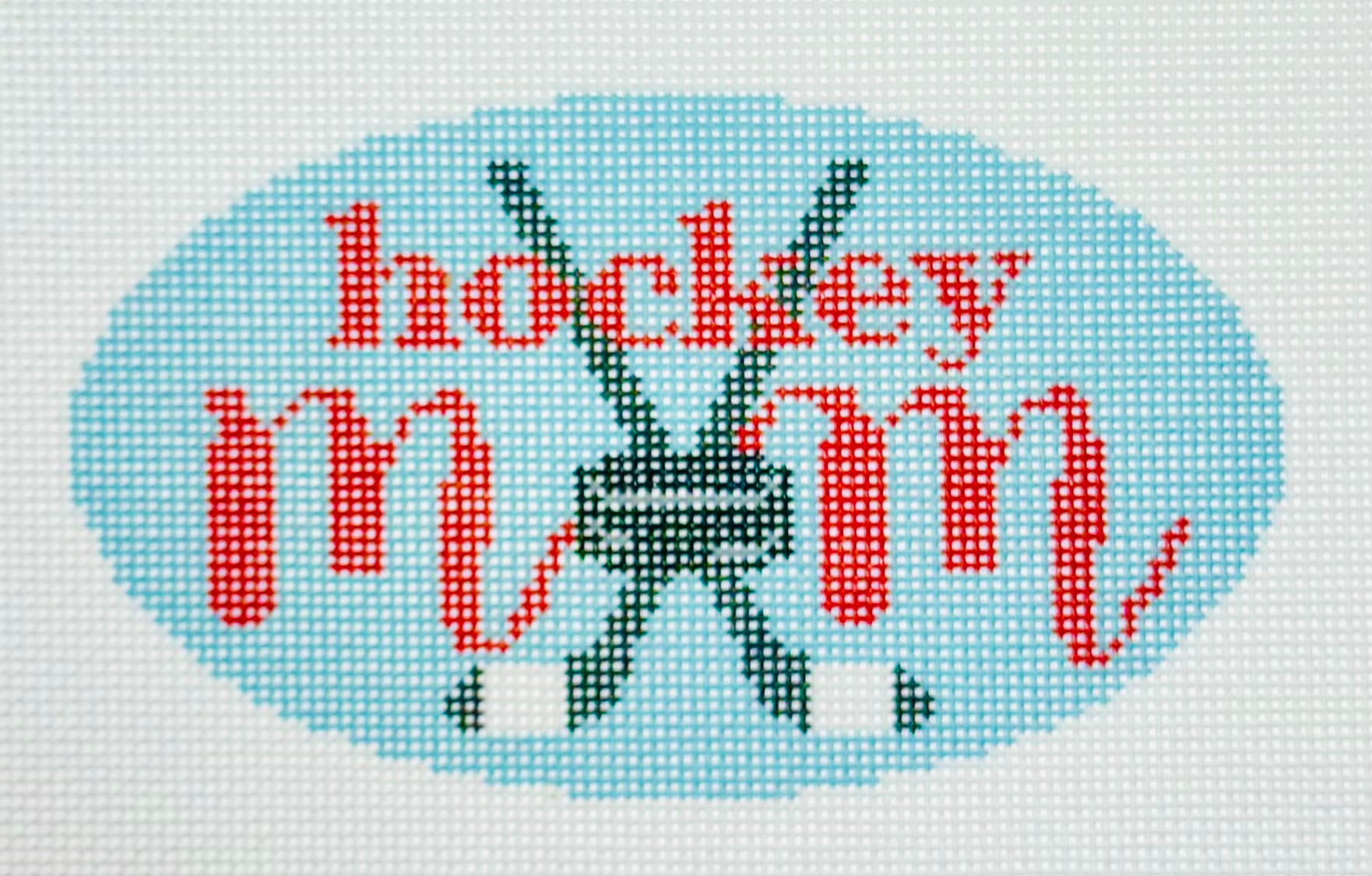 KCN Designers needlepoint canvas of 'Hockey Mom' with a hockey puck for the 'O' in 'mom' on a light blue background.