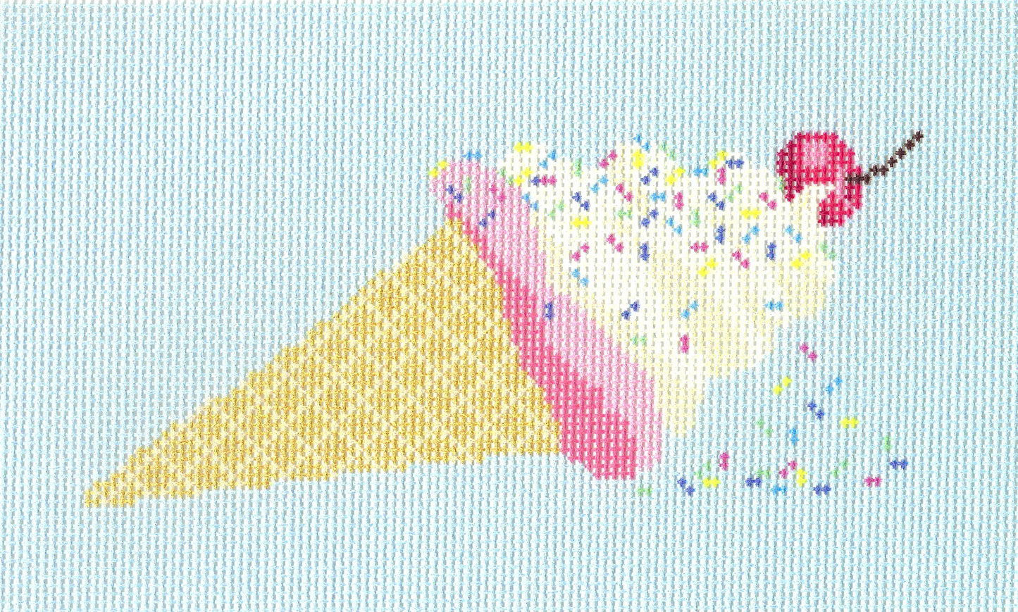 Needlepoint To Go needlepoint canvas of a waffle cone filled with white and pink ice cream, topped with a cherry and multicolored sprinkles, on a light blue background.