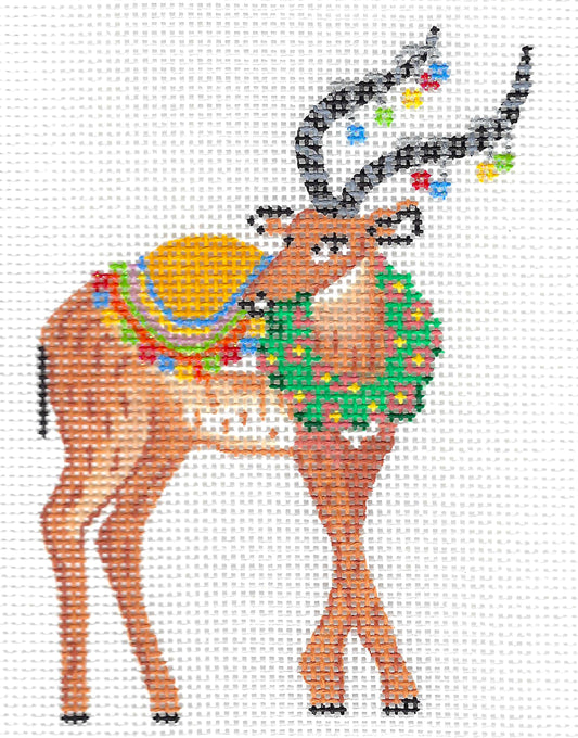 Kate Dickerson Needlepoint Collections needlepoint canvas of a festive brown reindeer with antlers decorated with colorful lights, a green wreath, and a yellow blanket on a white background.