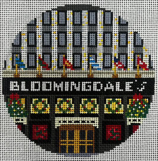 Gingham Stitchery circular needlepoint canvas of the words 'BERGDORT GODMAN' in a white sign above an arched doorway with yellow and orange window light, flanked by floral panels and gray side sections on a light background.